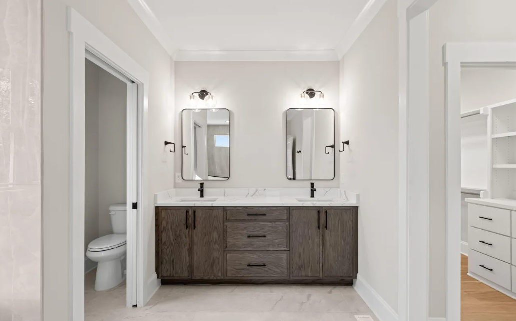 Modern white bathroom with double mirrors, dark wood vanity, and bright hallway view