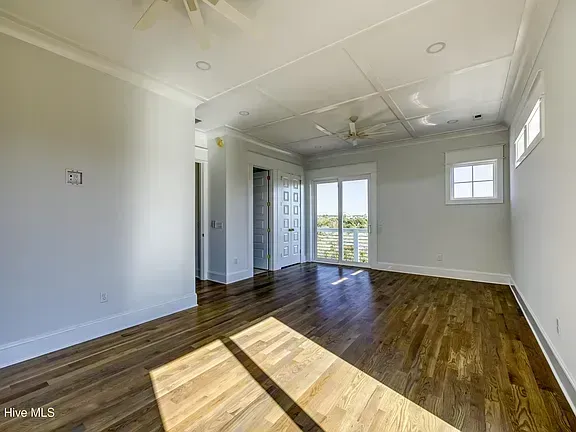Bright empty room with hardwood floors, white walls, and sunlight streaming through windows and glass doors