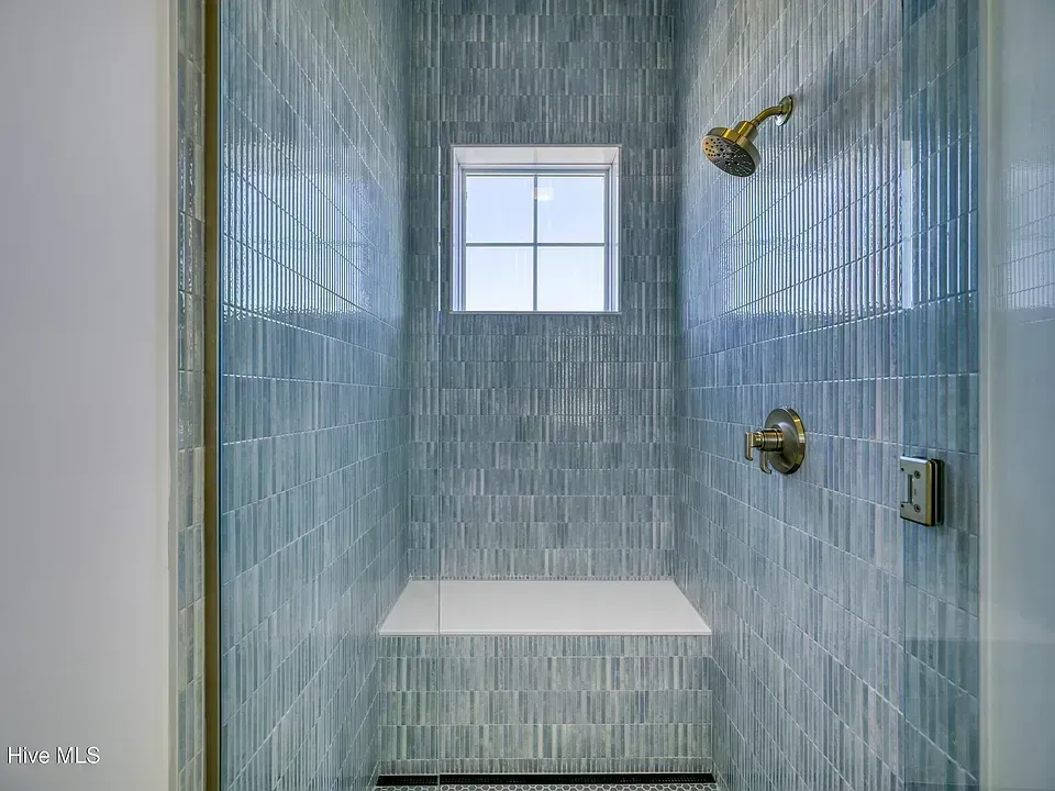 Empty blue-tiled shower with bench and small window.