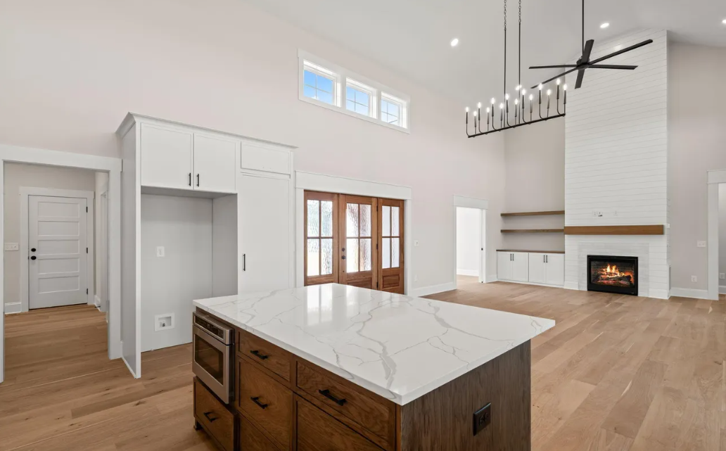 Bright modern kitchen and living room with white cabinets, wood floors, an island, a fireplace, and large windows