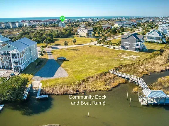 Aerial view of waterfront homes, grassy lawn, and community dock with boat ramp by the water