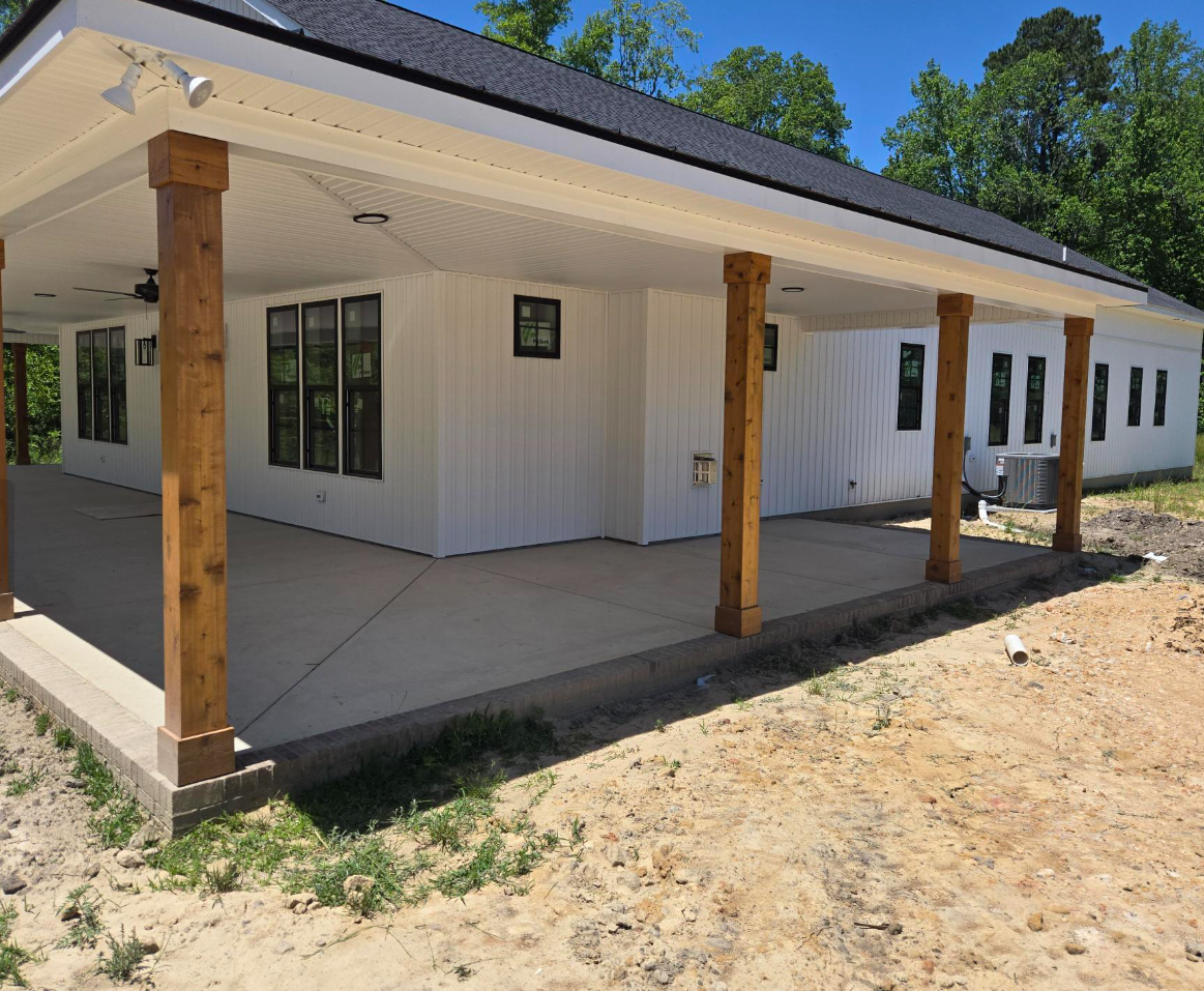 White house exterior with covered porch, wooden posts, and black-trimmed windows under construction