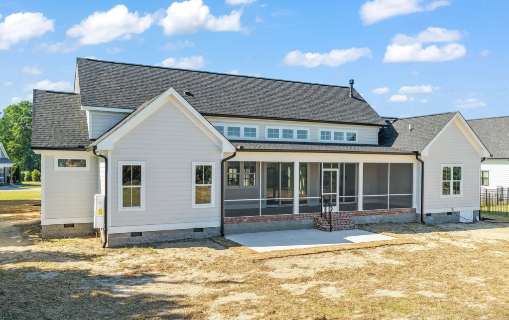 White single-story house with gray roof and front porch on a gravel lot under a blue sky