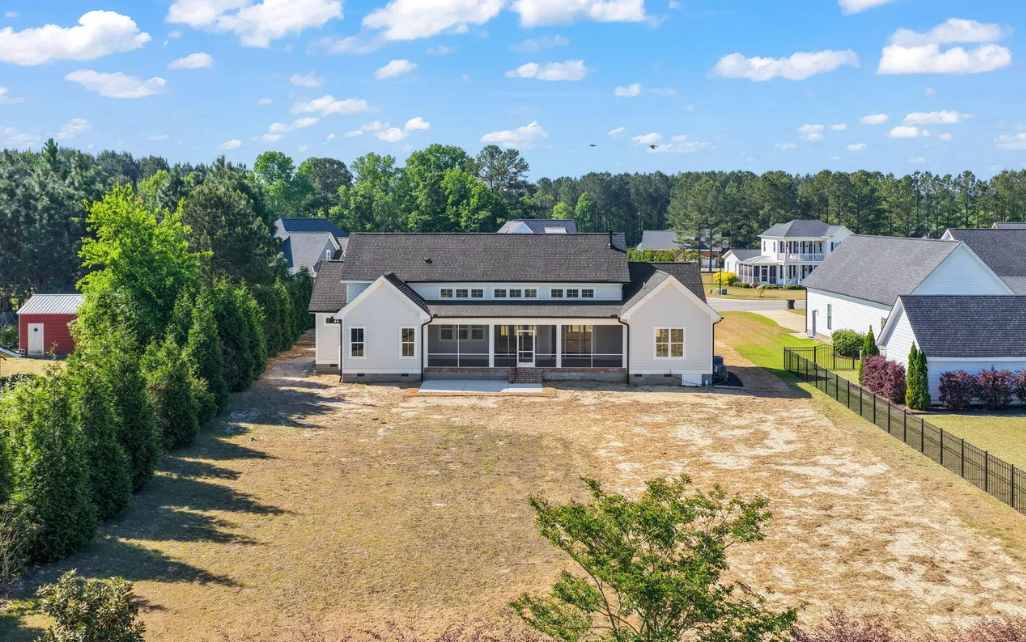 Aerial view of a large beige house with a wide dry yard, surrounded by trees and neighboring homes.