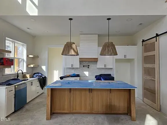 Modern kitchen with white cabinets, blue island, pendant lights, and a sliding barn door