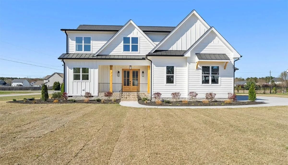 Modern white farmhouse with blue accents and a front porch on a rural lot