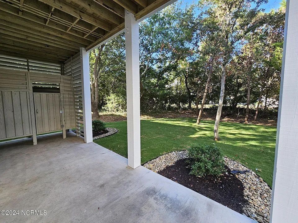 Covered patio with concrete floor, white posts, and a grassy backyard with trees.