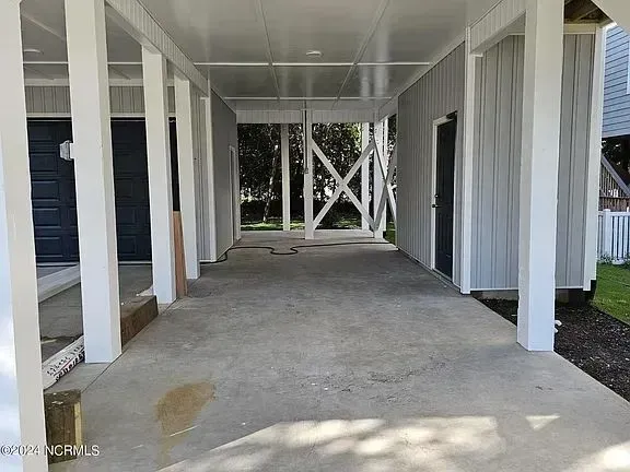 Covered concrete porch with white columns and cross-braced supports along a house exterior