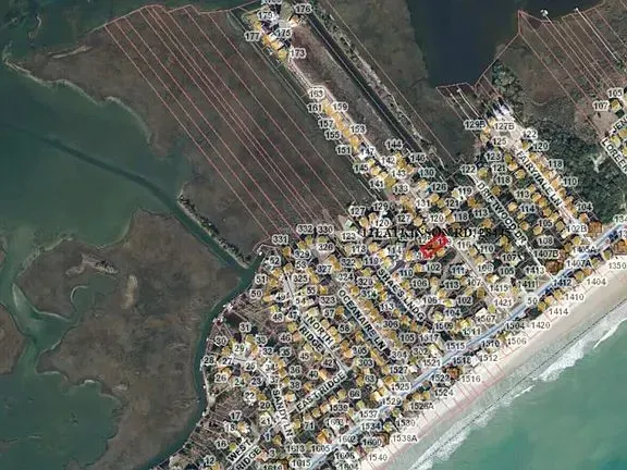 Aerial view of a coastal town with dense white buildings, farmland, and a sandy beach along turquoise water.