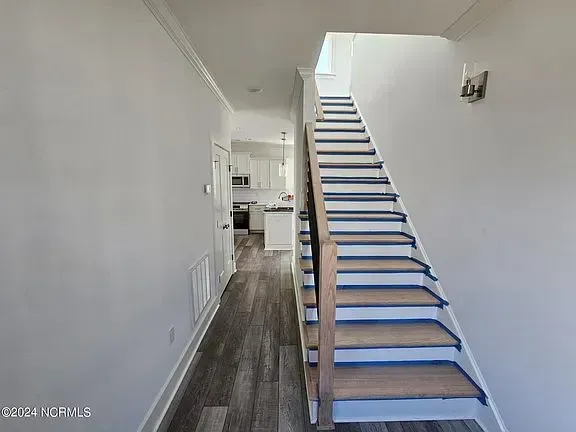 Narrow hallway with a carpeted staircase leading up, white walls, and wood flooring.