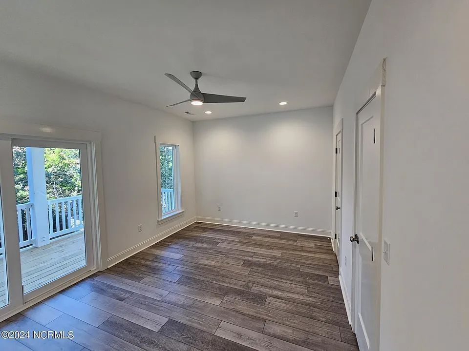 Empty modern room with wood flooring, white walls, ceiling fan, and sliding glass door to a deck