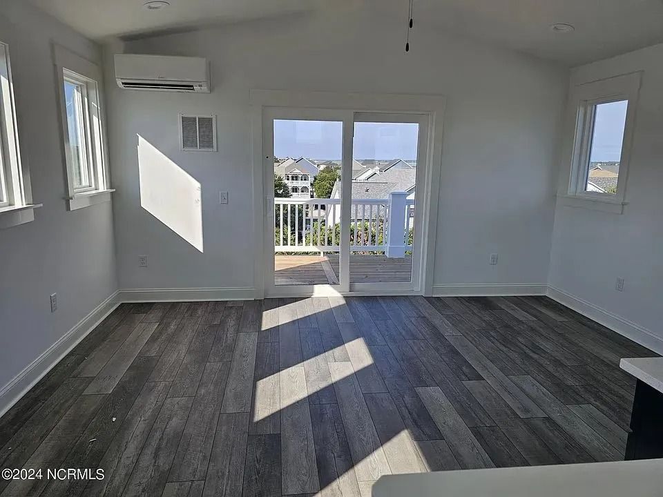 Empty bright room with gray wood floors, white walls, and sliding doors to a balcony.