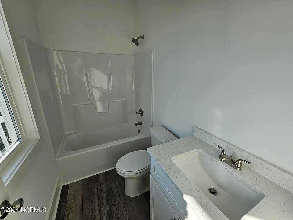 Small bathroom with white tub, toilet, and sink beside a window.