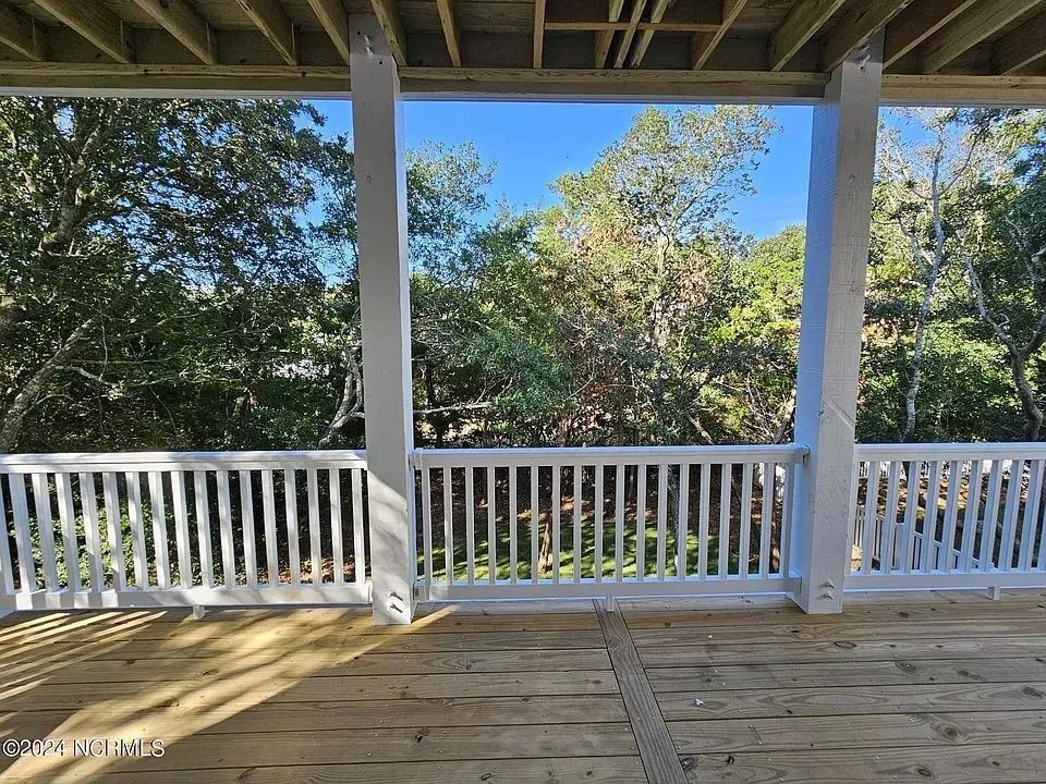 Covered porch with white railing, wooden deck floor, and trees beyond in bright daylight