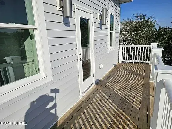 Wooden deck beside a gray house, with white railing, glass door, and window in bright sunlight