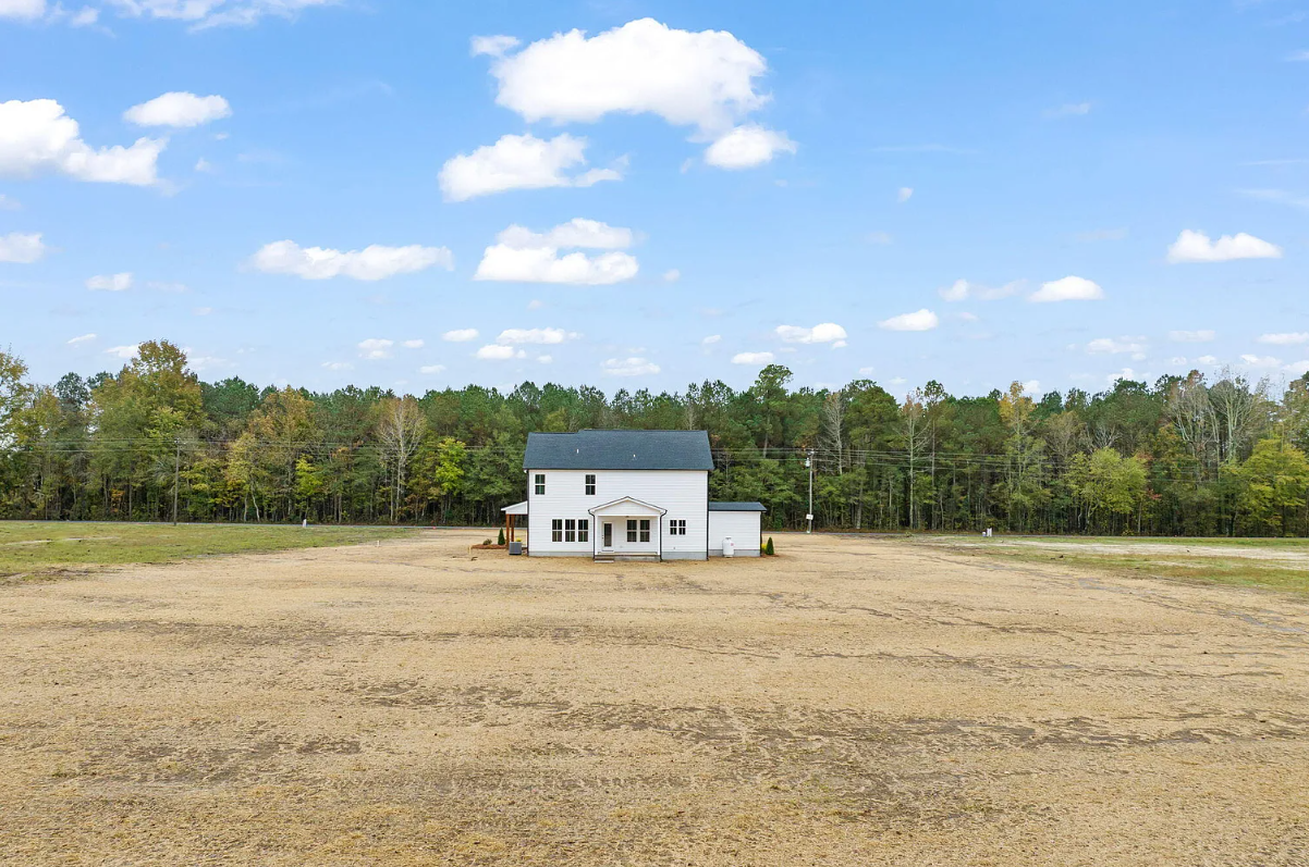 White house in a wide barren field with a tree line and blue sky with clouds in the background
