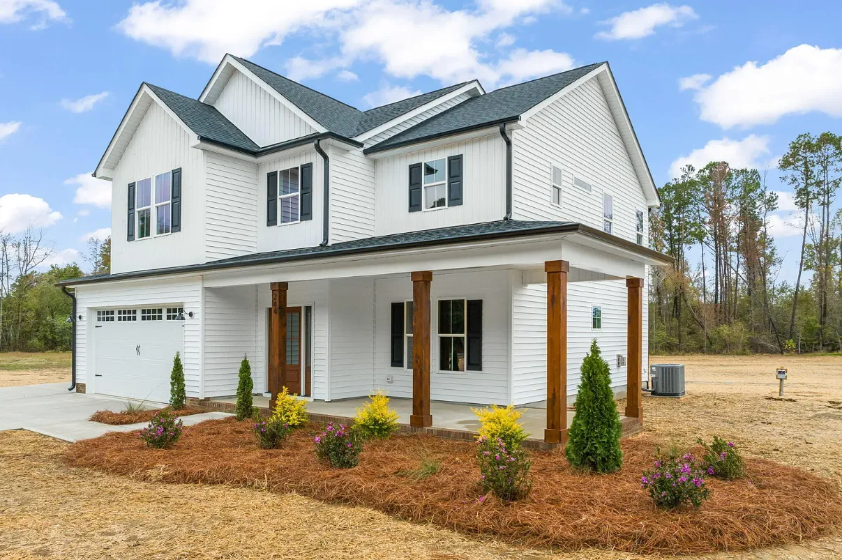 New white two-story house with a wraparound porch and garage in a landscaped yard