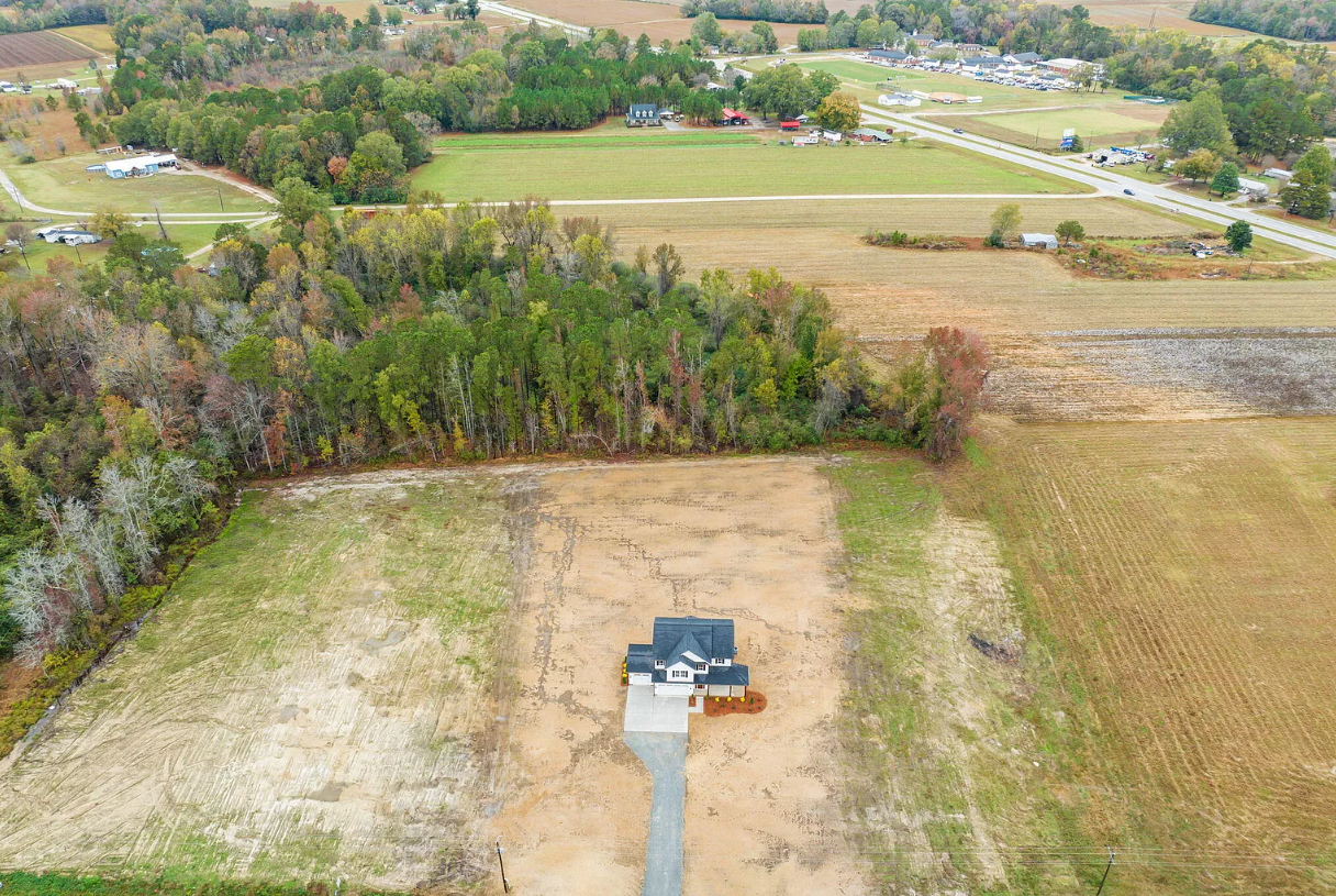 Aerial view of a rural lot with a house under construction and surrounding fields, trees, and road.