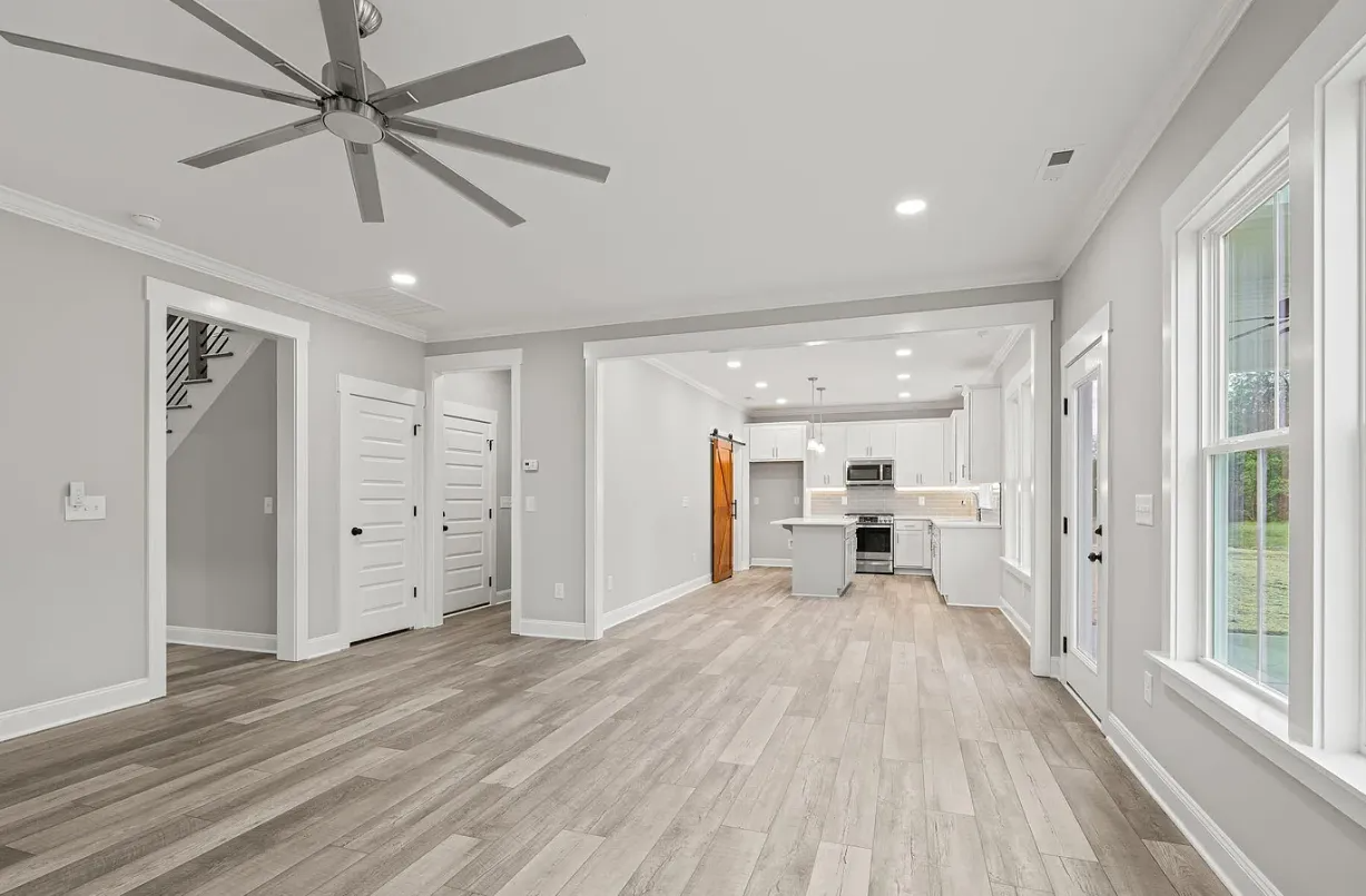 Bright open-plan living room and kitchen with gray wood floors, white walls, and large windows