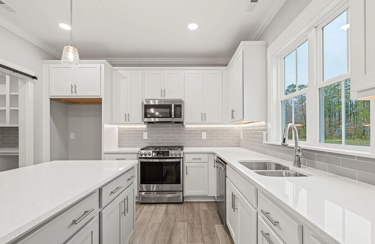 Bright white modern kitchen with stainless steel appliances, large window, and marble countertops
