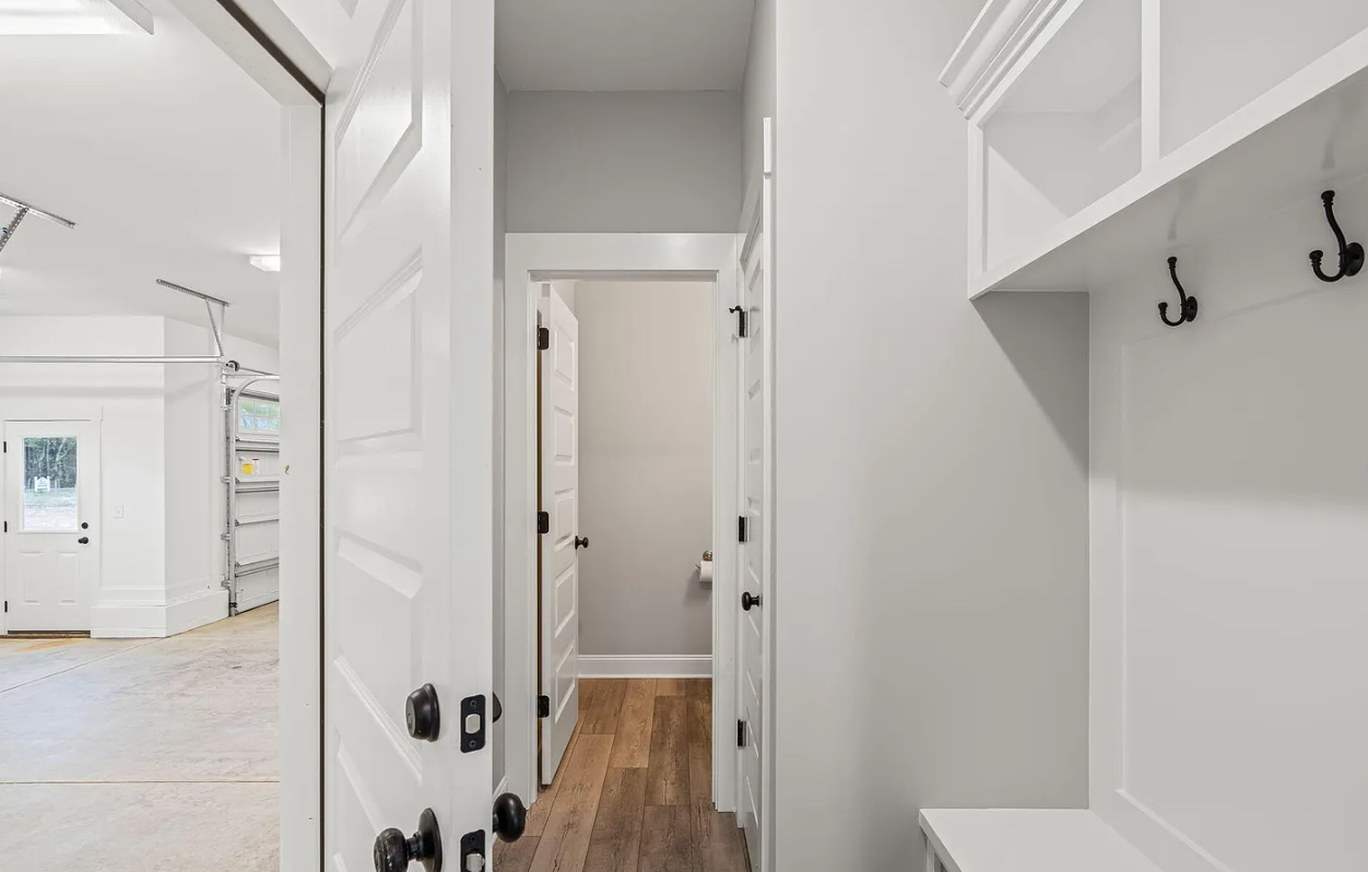 White hallway with wood floor, open door, and built-in coat hooks and shelves.