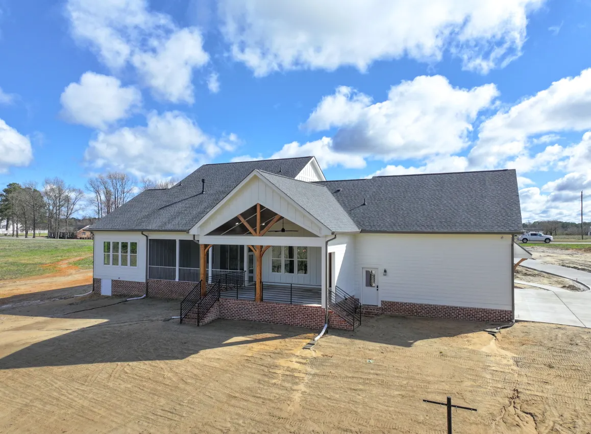 New white house under construction with a front porch and gray roof on a dirt lot