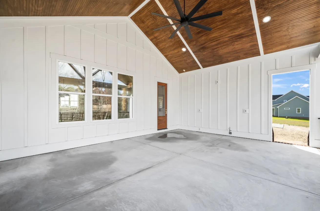 Empty modern room with white paneled walls, concrete floor, vaulted wood ceiling, and large windows