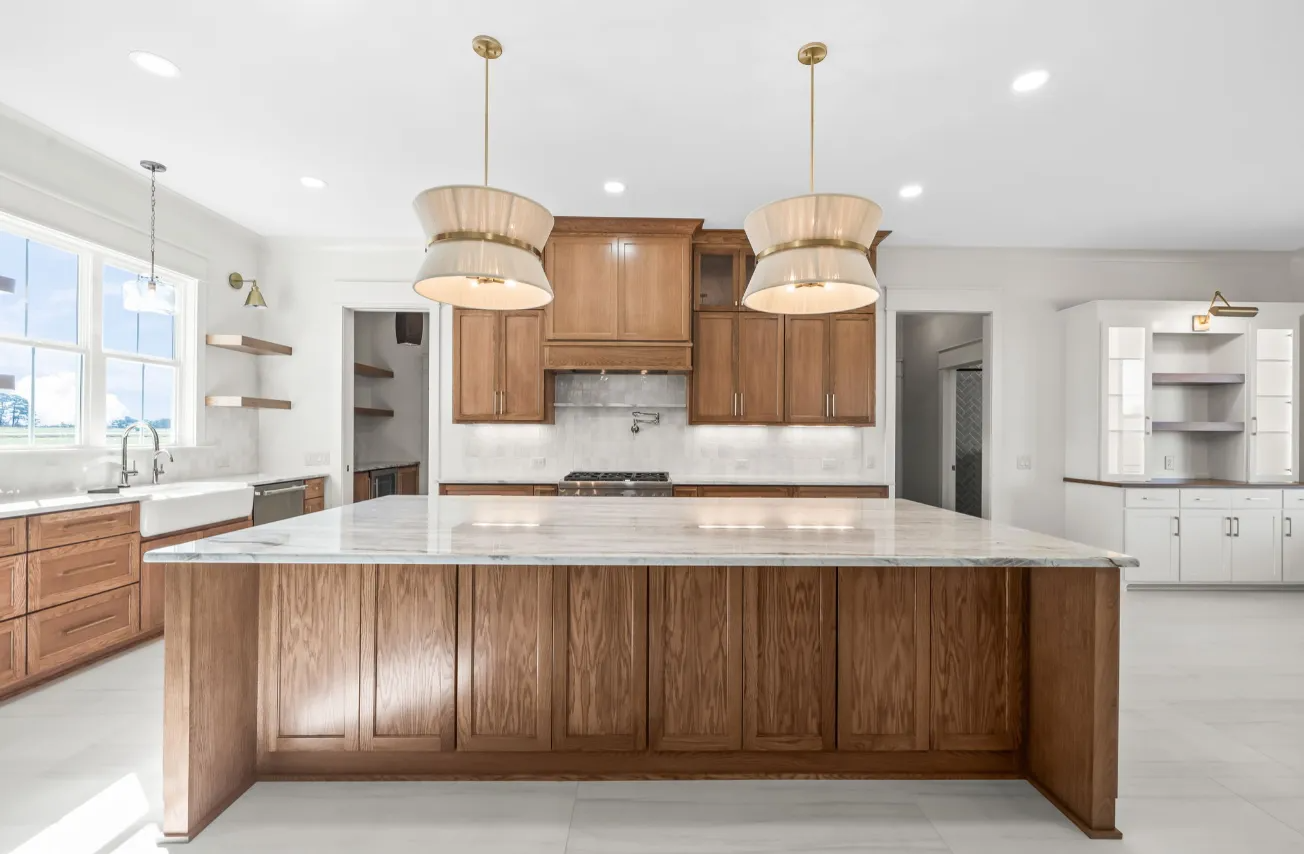 Bright modern kitchen with white island, wood cabinets, marble counters, and pendant lights