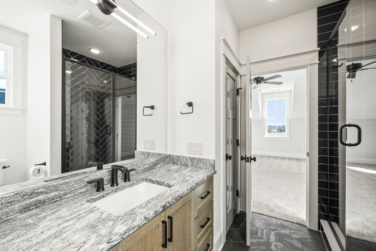 Modern bathroom with granite double vanity, large mirror, black shower tile, and glass shower door