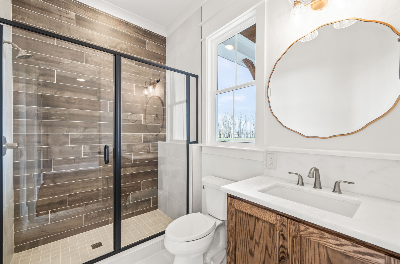 Modern bathroom with glass shower, wood vanity, and oval mirror