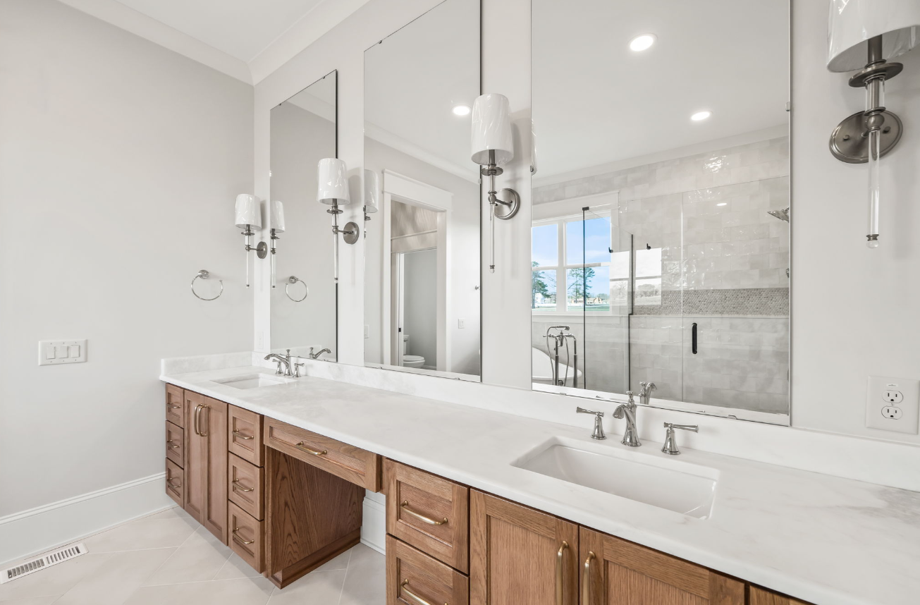 Bright bathroom with double vanity, large mirrors, white countertops, and wood cabinets