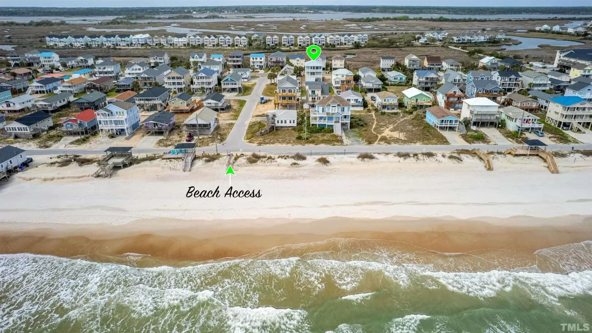 Aerial view of beach houses and dunes beside a wide sandy shoreline and ocean waves