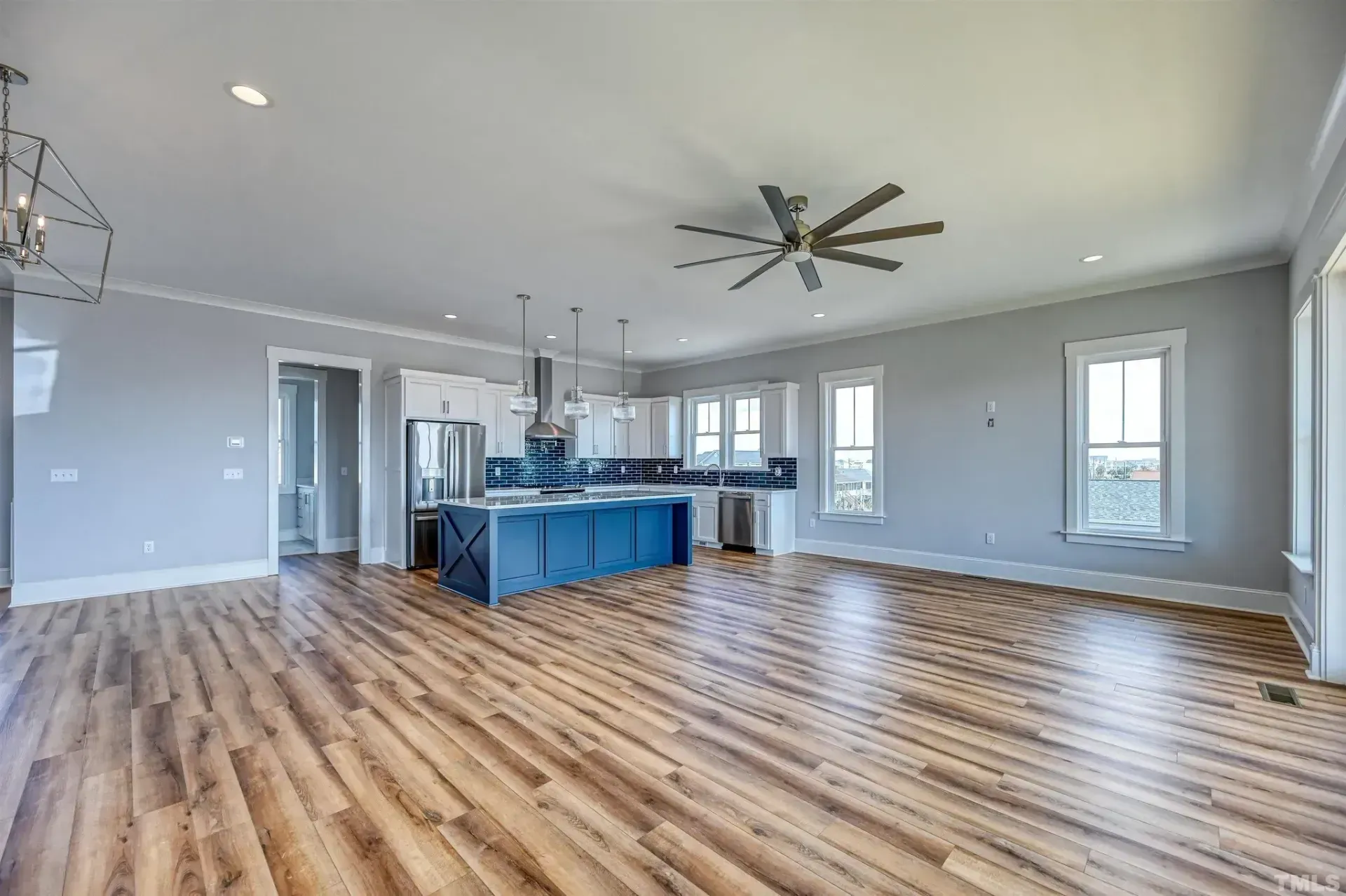 Spacious modern living room with light wood floors, gray walls, and a blue kitchen island under a ceiling fan