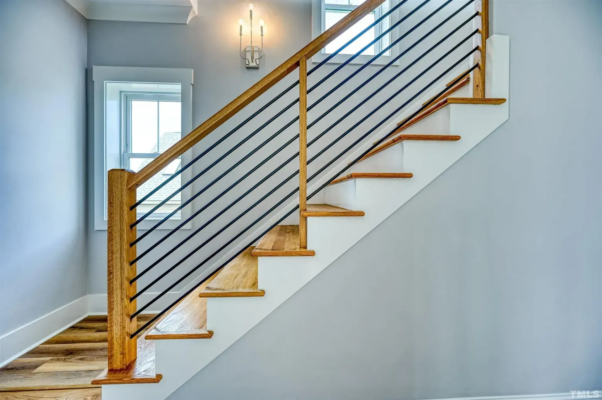 Modern staircase with wood steps, cable railing, and light gray walls in a bright hallway