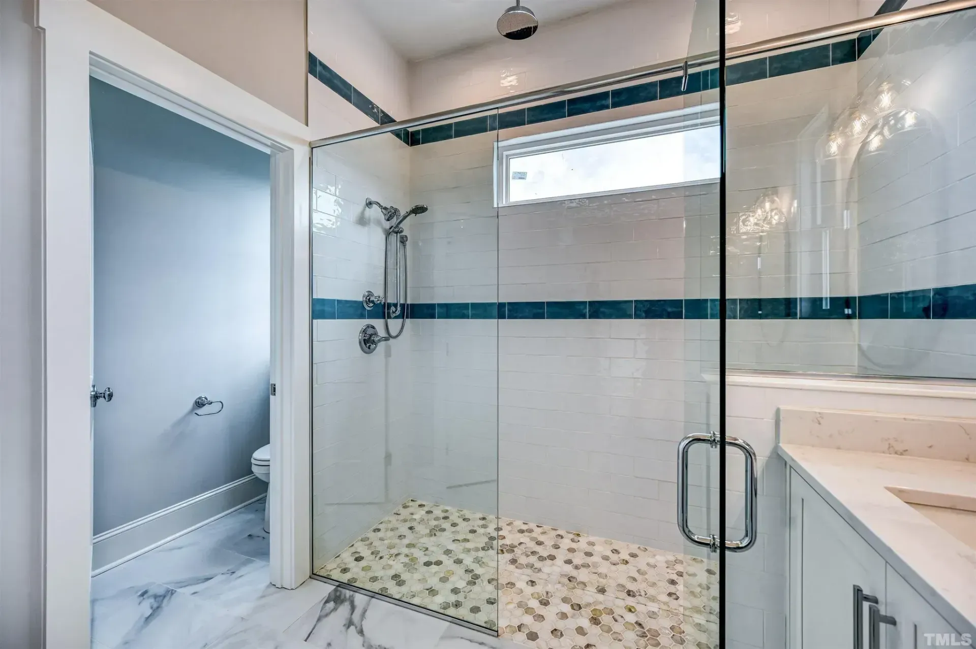 Bright bathroom with glass walk-in shower, white tile, and blue accent band