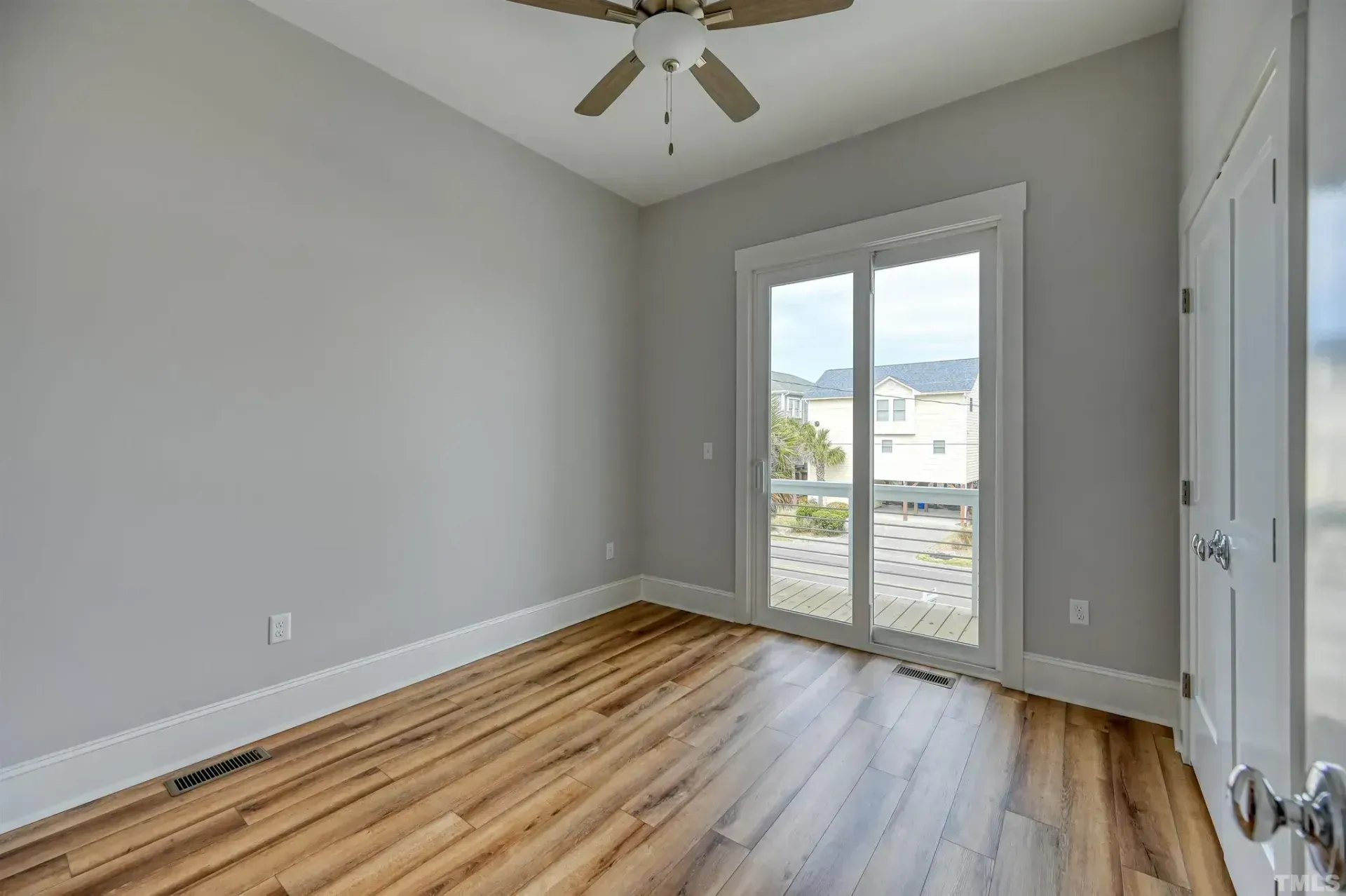 Empty bedroom with gray walls, wood floors, ceiling fan, and glass doors to a balcony.