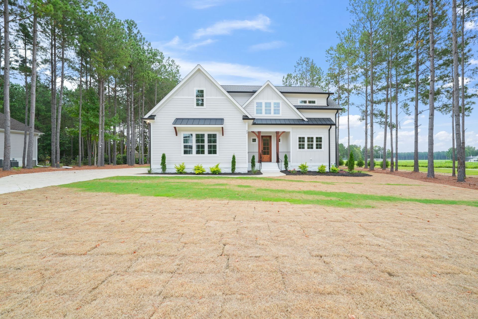 Modern white house with gabled roof, front porch, and large lawn beside tall pine trees