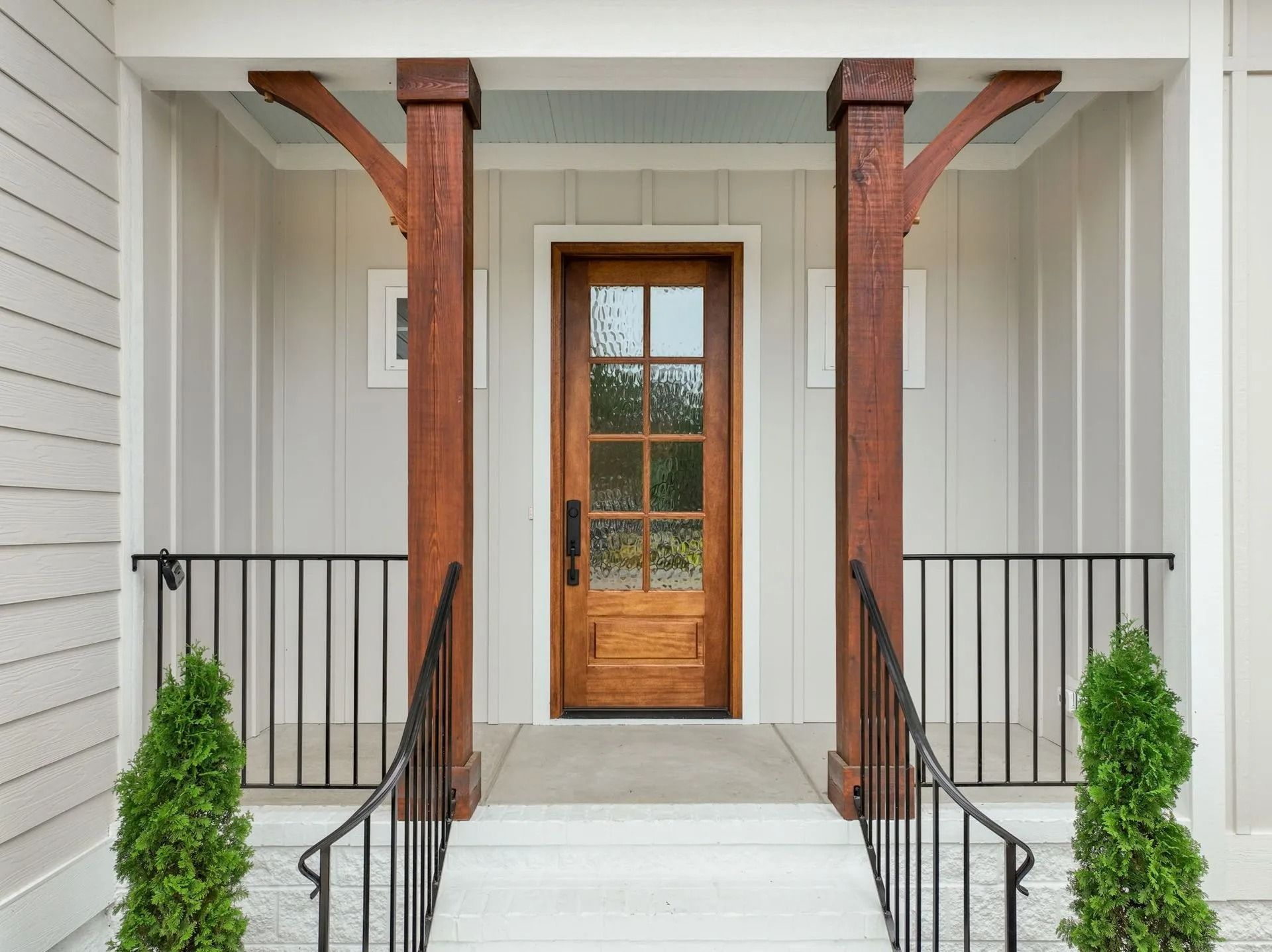 Front porch with white steps, black railings, and a wooden front door framed by two rustic columns.