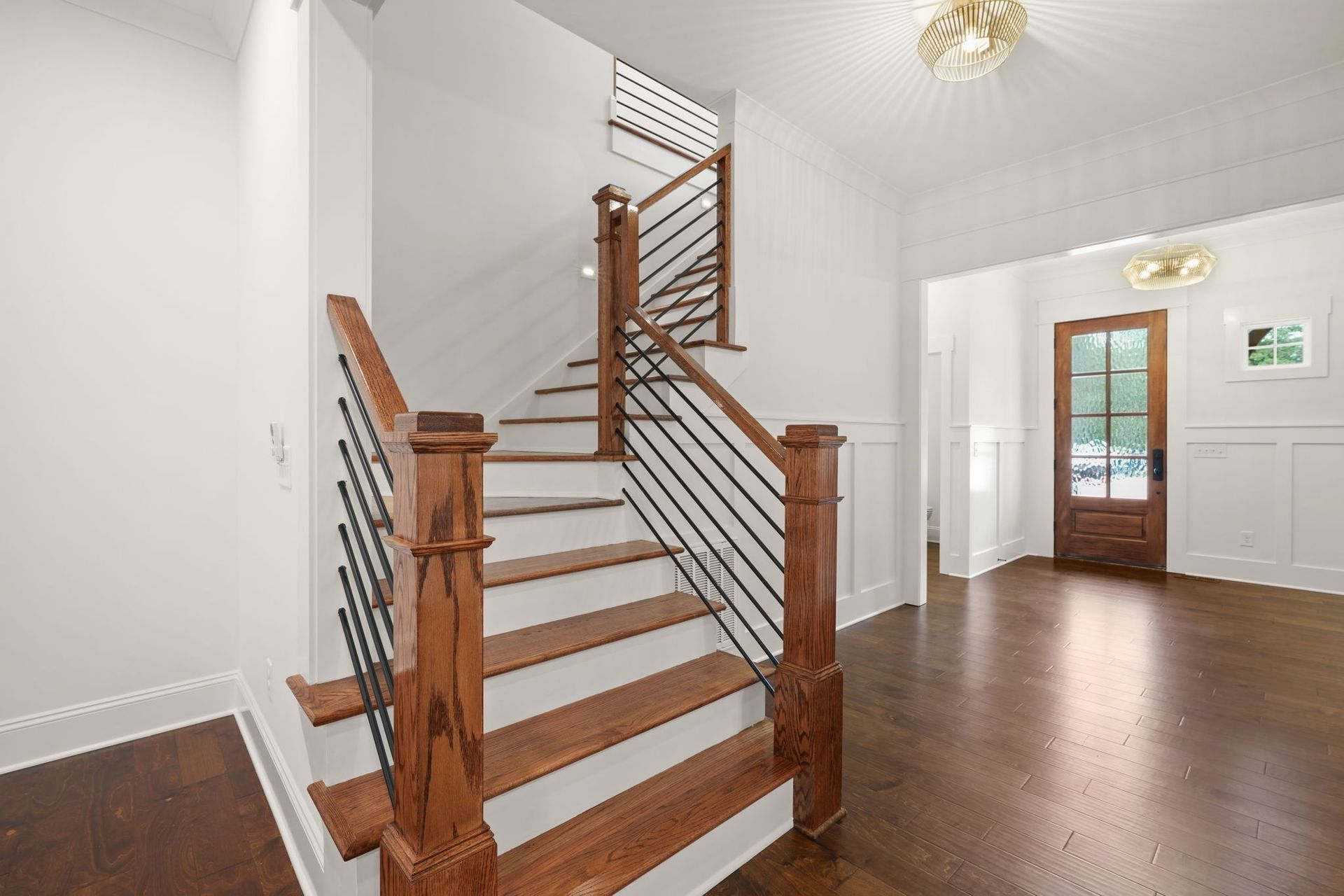 Bright foyer with wooden staircase, white walls, hardwood floors, and a front door.