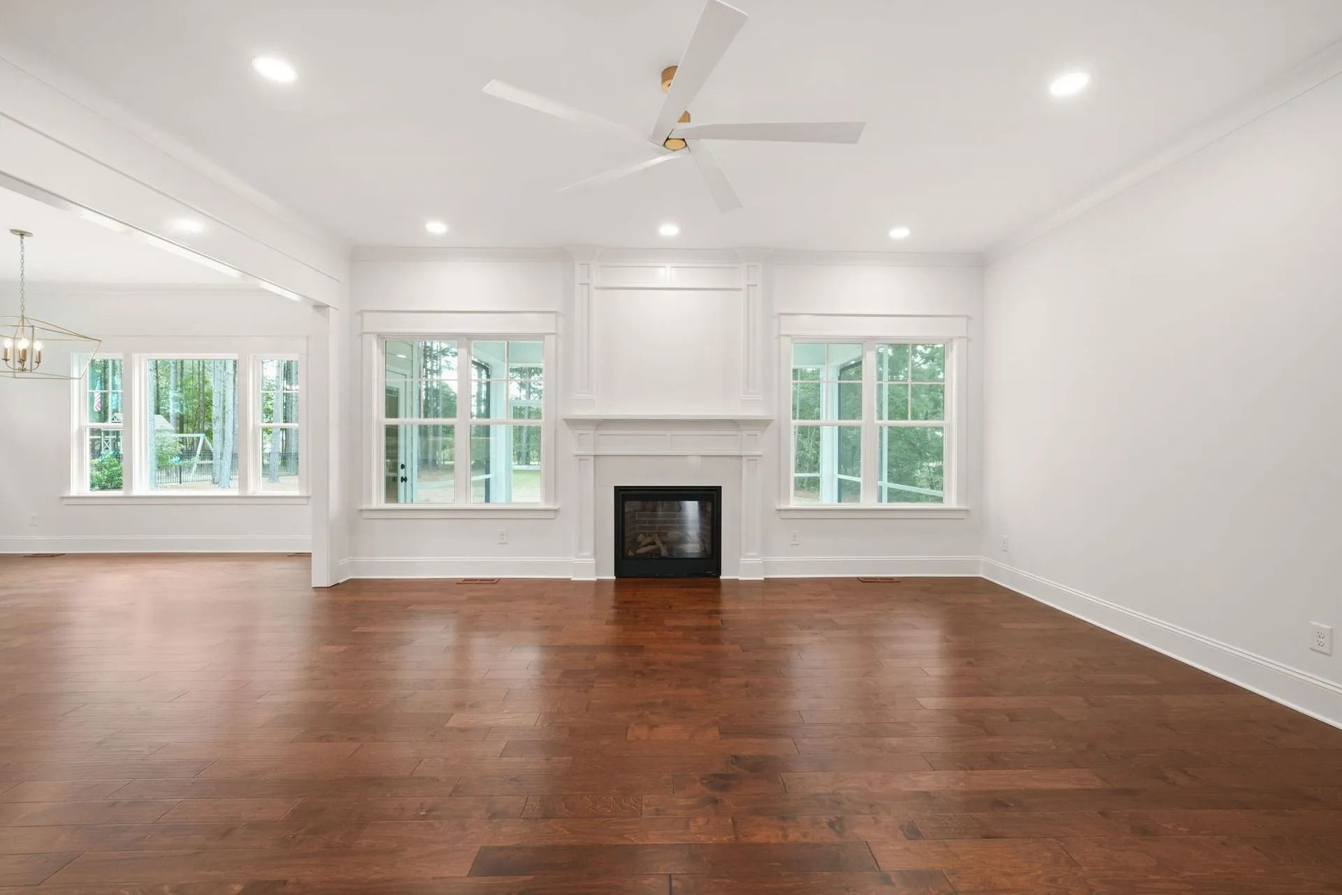 Empty bright living room with hardwood floors, white walls, a fireplace, and large windows