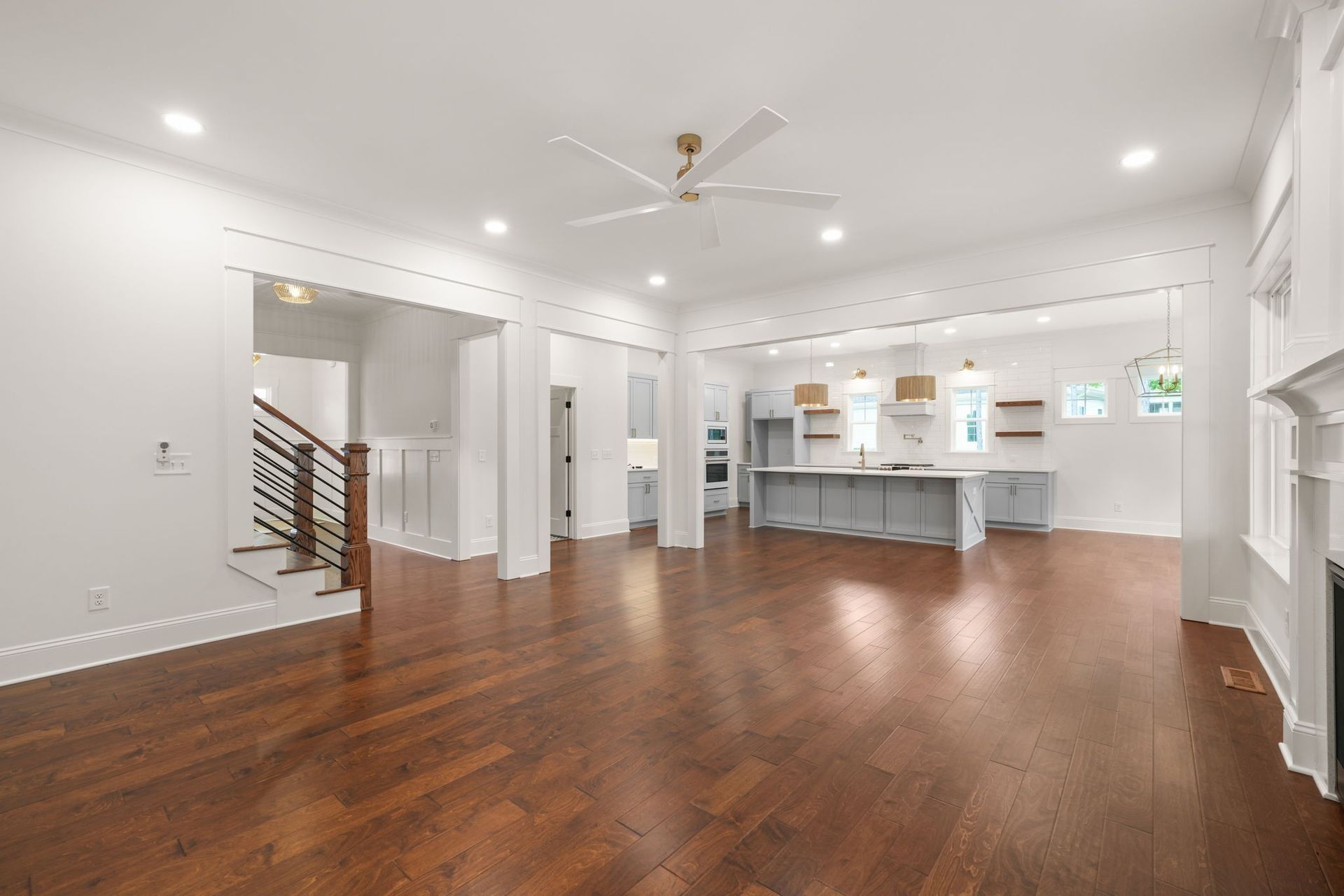 Spacious empty open-plan living area with hardwood floors, white walls, and a modern kitchen counter.