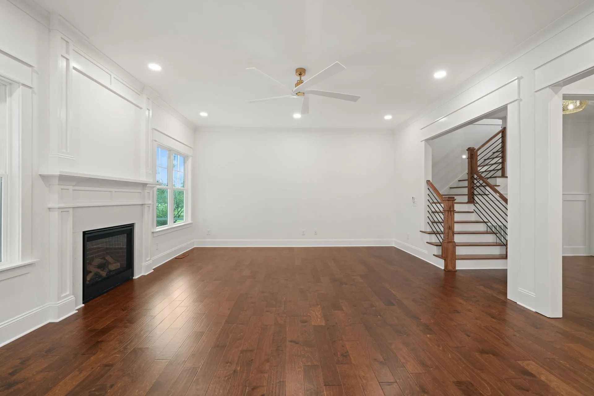 Empty bright living room with hardwood floors, white walls, fireplace, and staircase to the right