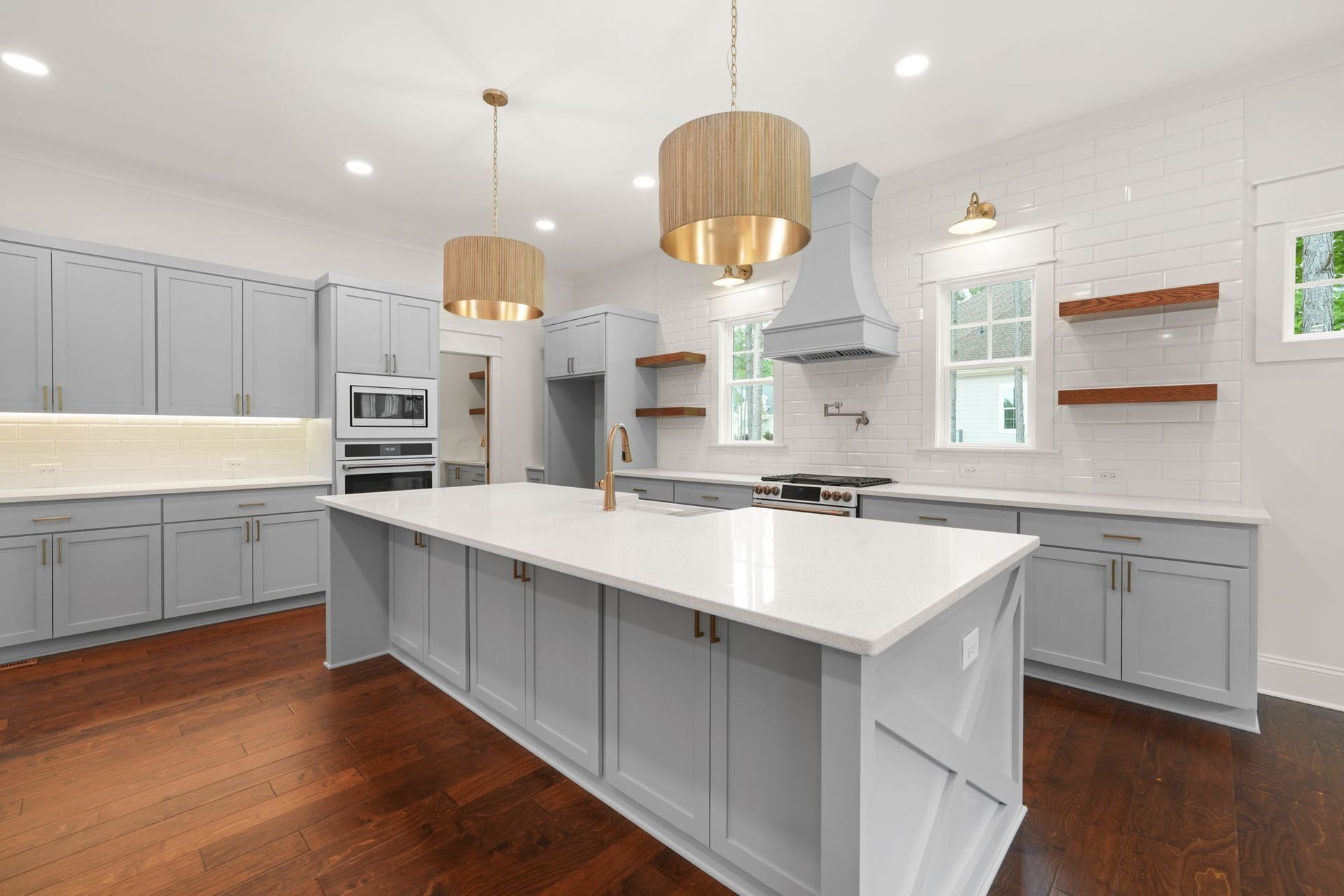 Bright modern kitchen with gray cabinets, white island, wood floors, and pendant lights