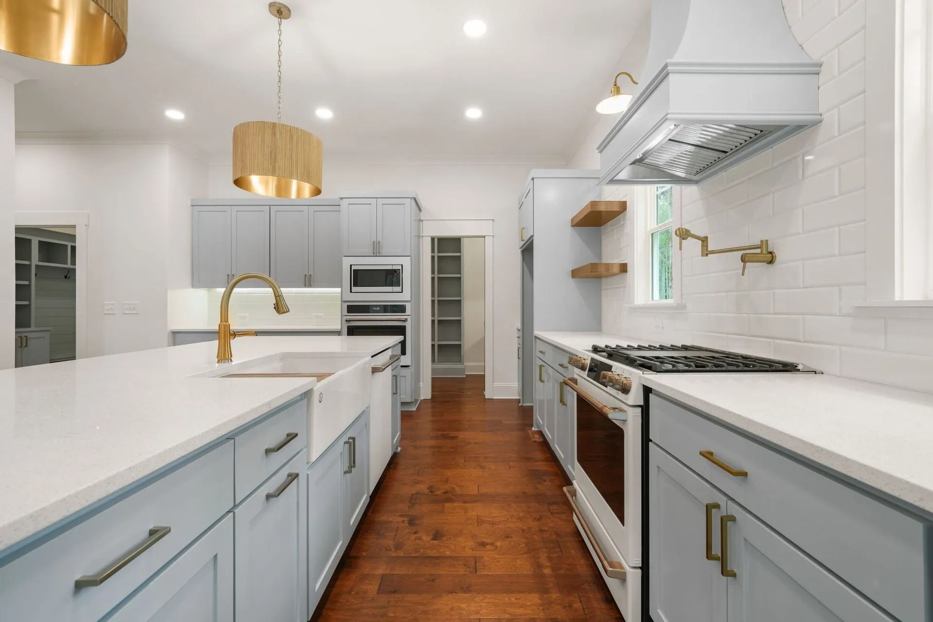 Bright modern kitchen with white cabinets, gold pendant lights, and blue island cabinets