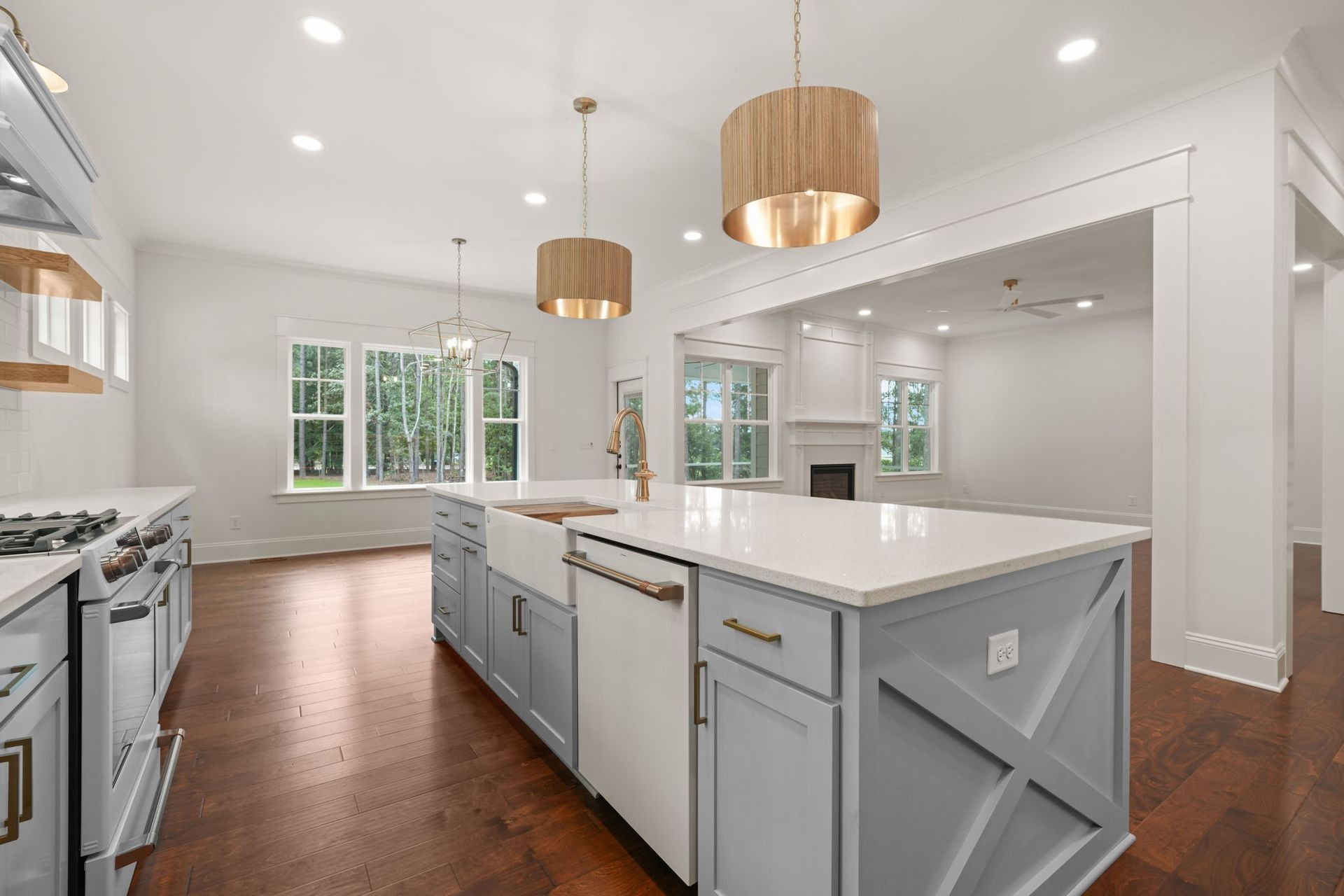 Bright modern kitchen with white cabinets, island, wood floors, and pendant lights near large windows