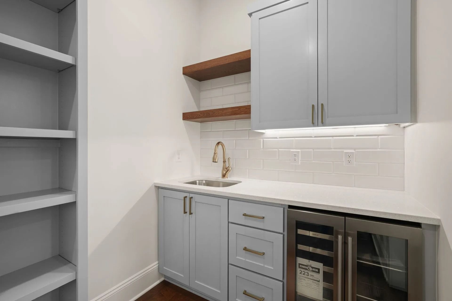 Small modern kitchen with gray cabinets, open shelves, white backsplash, and a sink with wine cooler.