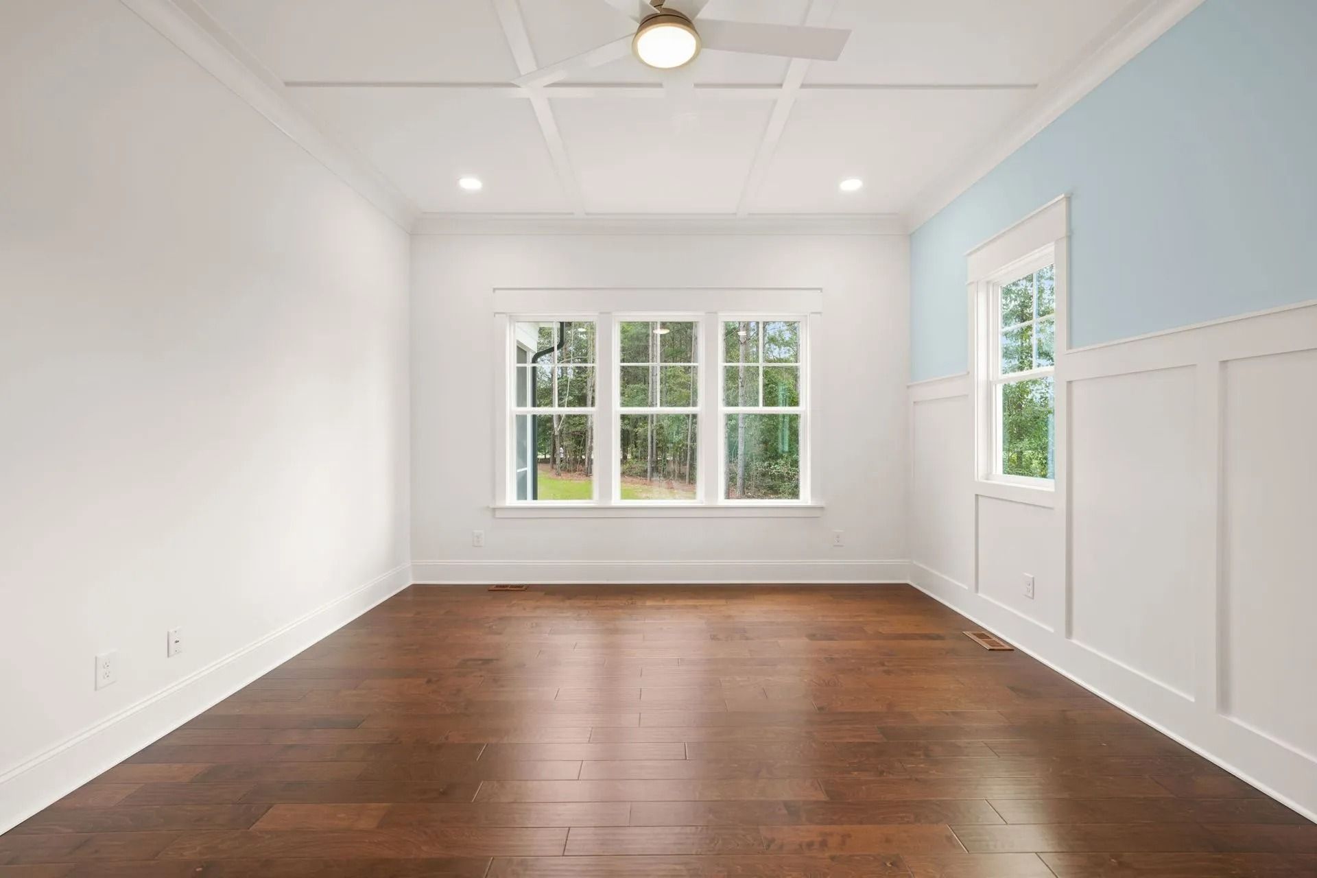 Bright empty room with hardwood floors, white walls, and large windows letting in daylight