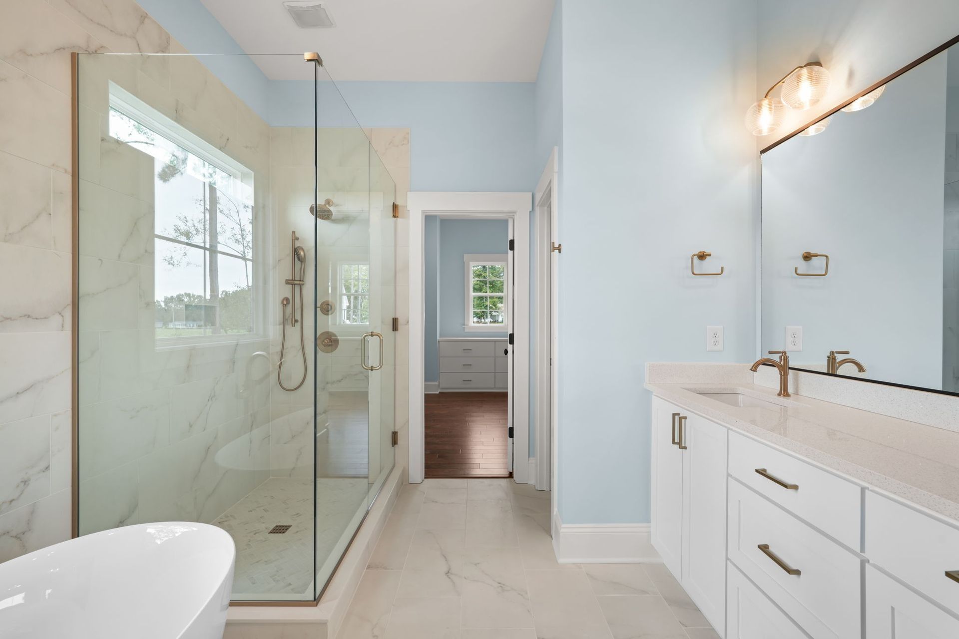 Bright modern bathroom with glass shower, double vanity, and light blue walls