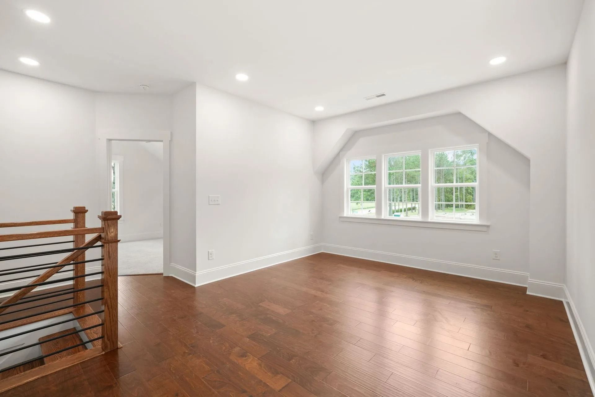 Empty bright room with hardwood floors, white walls, and a large window nook.