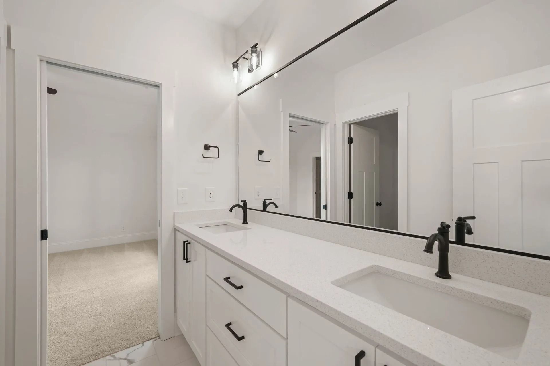 Modern white bathroom with double vanity, black faucets, and a large mirror